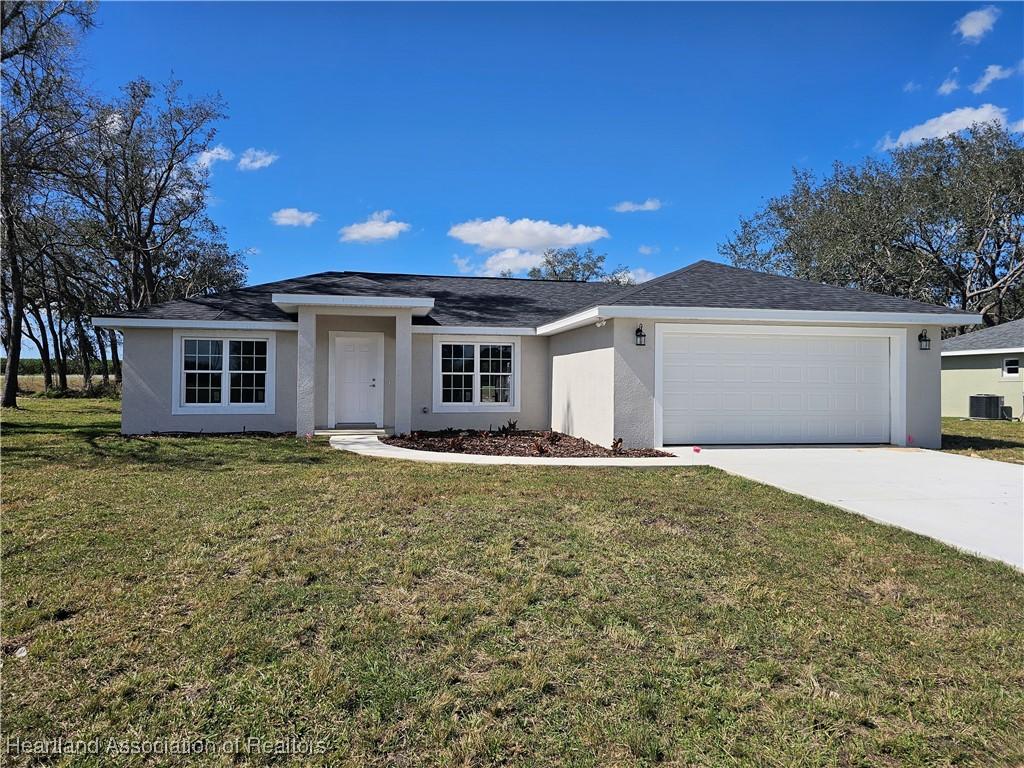 view of front of home with a garage, a front yard, and central AC unit