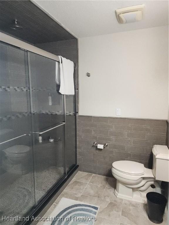 full bath featuring tile walls, a shower stall, wainscoting, and tile patterned flooring