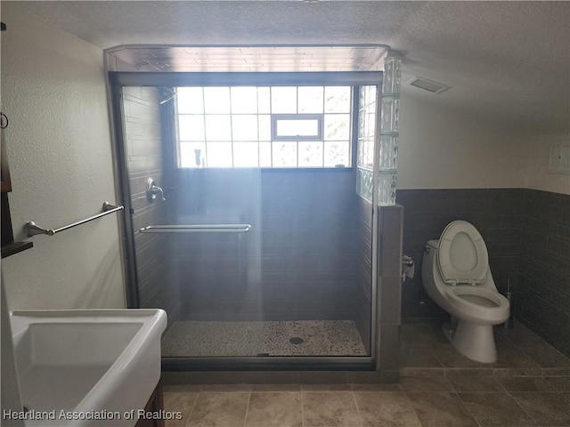 bathroom with a shower stall, a textured ceiling, tile patterned flooring, tile walls, and a wainscoted wall