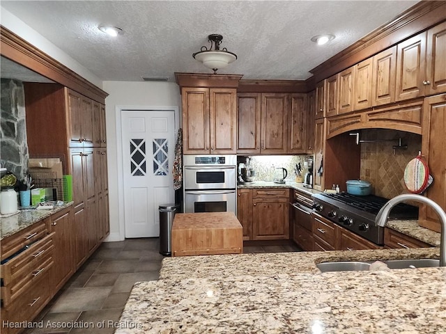 kitchen with stainless steel double oven, tasteful backsplash, light stone countertops, a textured ceiling, and brown cabinetry