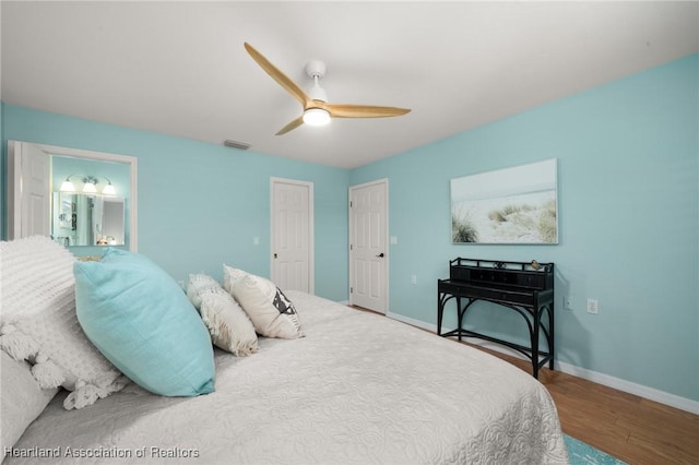 bedroom featuring connected bathroom, a ceiling fan, visible vents, baseboards, and wood finished floors