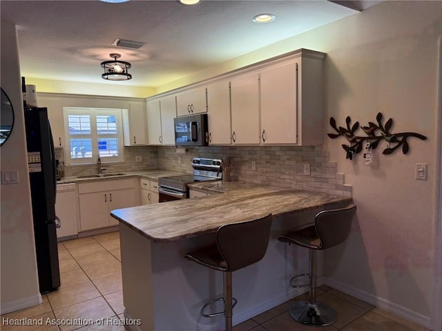 kitchen featuring light tile patterned flooring, a peninsula, appliances with stainless steel finishes, and a sink
