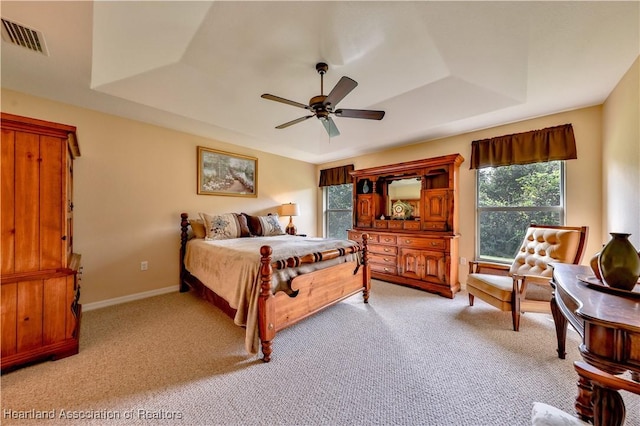 carpeted bedroom with a raised ceiling and ceiling fan