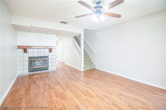 unfurnished living room with a tile fireplace, ceiling fan, light hardwood / wood-style floors, and a textured ceiling