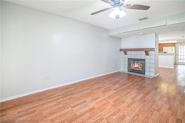 unfurnished living room with ceiling fan, light hardwood / wood-style floors, a textured ceiling, and a tiled fireplace