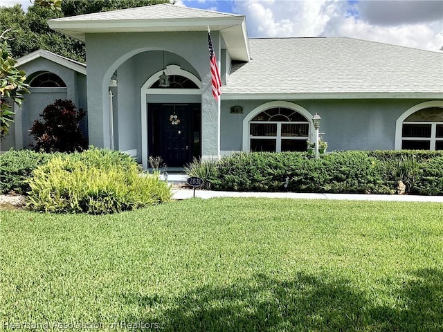 2831 Sunrise Dr, Sebring, FL 33872 - view of exterior entry with a lawn, a shingled roof, and stucco siding