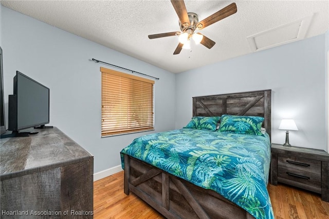bedroom with a textured ceiling, attic access, a ceiling fan, baseboards, and wood finished floors