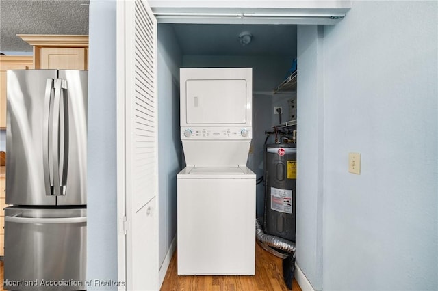 laundry area with laundry area, water heater, wood finished floors, and stacked washer / dryer