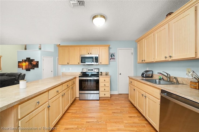 kitchen featuring visible vents, a sink, appliances with stainless steel finishes, and light brown cabinetry