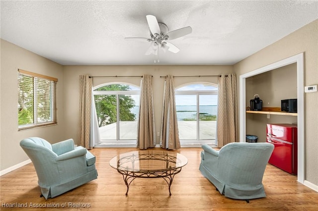 sitting room featuring a textured ceiling, ceiling fan, baseboards, and wood finished floors