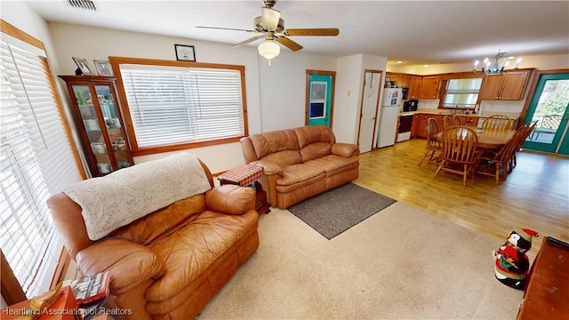 living room featuring light wood-type flooring, ceiling fan with notable chandelier, and a wealth of natural light