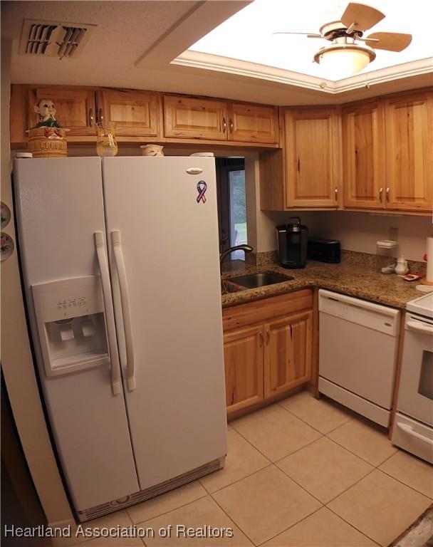 kitchen featuring visible vents, dark stone countertops, light tile patterned flooring, white appliances, and a sink