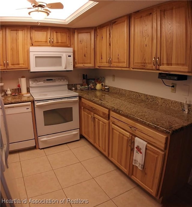 kitchen with white appliances, light tile patterned floors, dark stone countertops, and ceiling fan