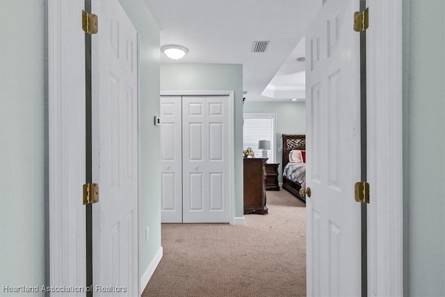 corridor featuring a raised ceiling and light colored carpet