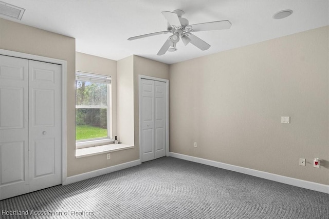 unfurnished bedroom featuring ceiling fan, carpet floors, and multiple closets