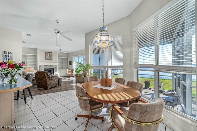 dining room with light tile patterned floors, a fireplace, ceiling fan with notable chandelier, and visible vents
