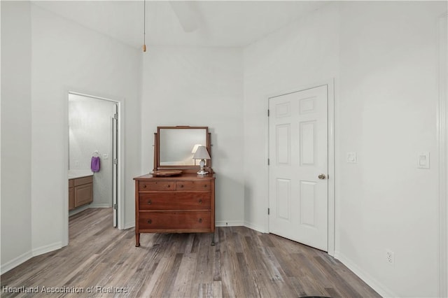 bedroom with baseboards, ensuite bath, and wood finished floors