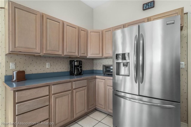 kitchen featuring light brown cabinetry, a toaster, dark countertops, stainless steel refrigerator with ice dispenser, and light tile patterned floors