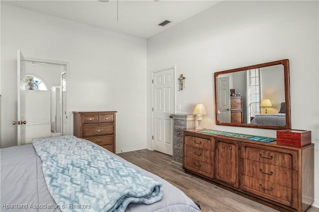 bedroom with visible vents, attic access, baseboards, and wood finished floors