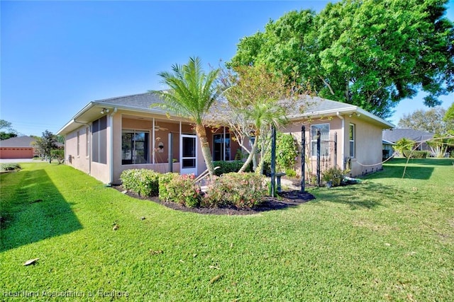 rear view of property featuring a yard, a sunroom, and stucco siding