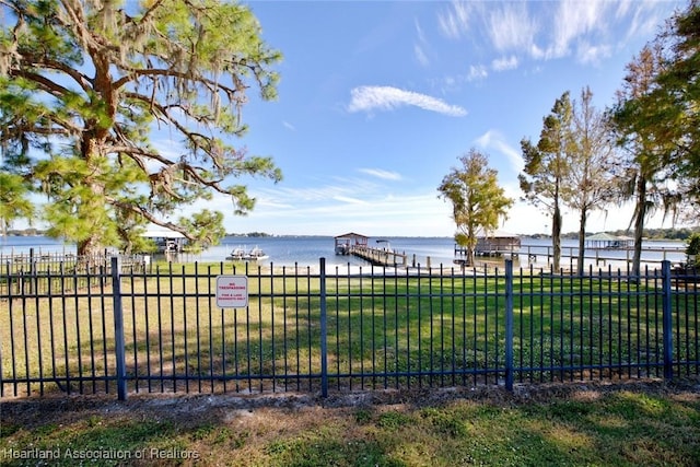 view of property's community with a lawn, fence, a water view, and a boat dock