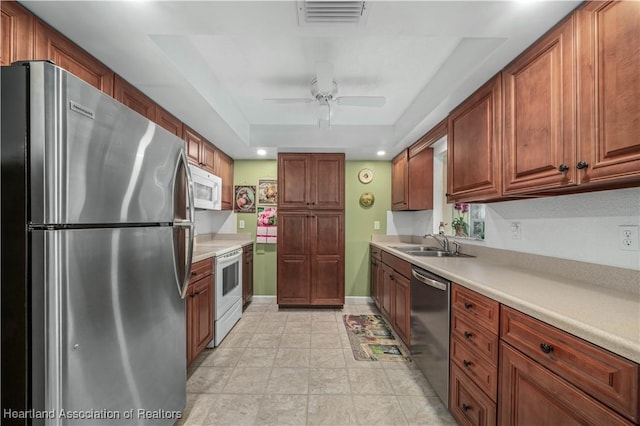 kitchen with appliances with stainless steel finishes, a tray ceiling, ceiling fan, and sink