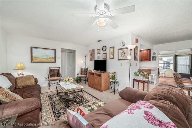 living room with a textured ceiling, light colored carpet, and ceiling fan