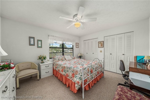 bedroom featuring ceiling fan, light colored carpet, a textured ceiling, and multiple closets