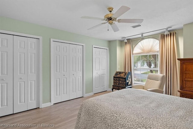 bedroom featuring rail lighting, ceiling fan, light hardwood / wood-style flooring, and multiple closets