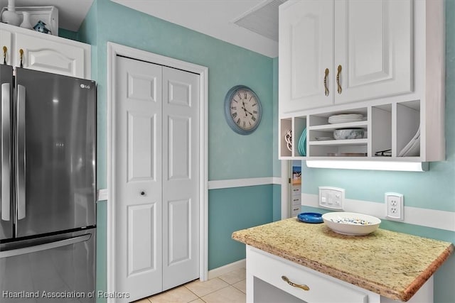 kitchen featuring white cabinets, stainless steel fridge, light stone counters, and light tile patterned flooring