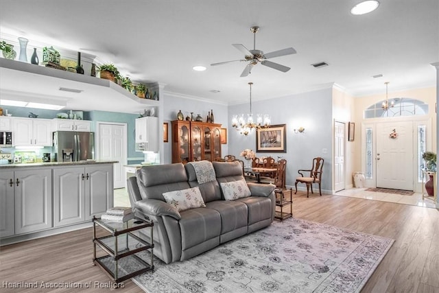 living room featuring ceiling fan with notable chandelier, light wood-type flooring, and crown molding