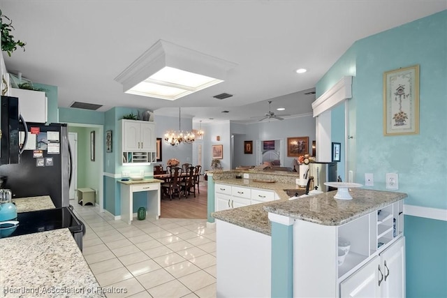 kitchen with black refrigerator, ceiling fan with notable chandelier, light tile patterned floors, white cabinets, and a center island