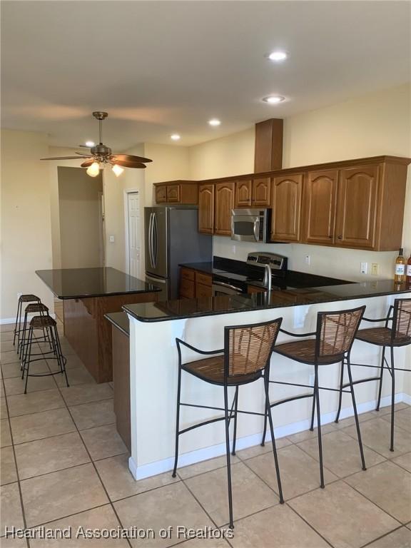 kitchen with a ceiling fan, dark countertops, appliances with stainless steel finishes, a breakfast bar, and a peninsula