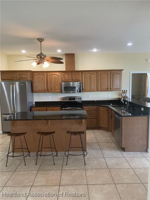 kitchen featuring ceiling fan, light tile patterned floors, a sink, appliances with stainless steel finishes, and a kitchen bar