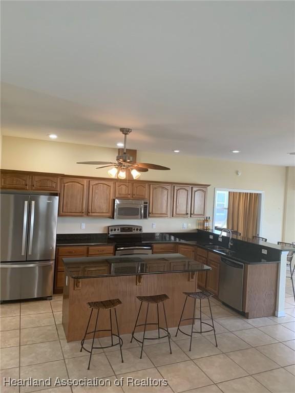 kitchen featuring dark countertops, appliances with stainless steel finishes, a sink, a peninsula, and a kitchen bar