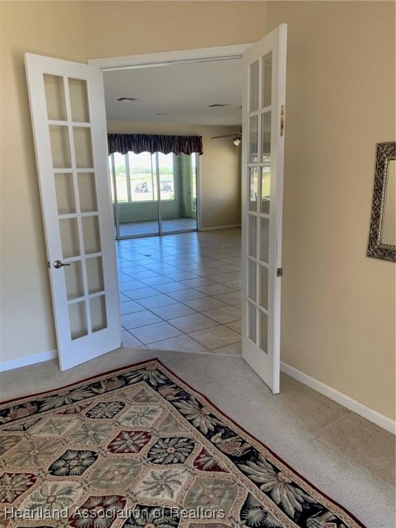 hallway with light tile patterned floors, baseboards, light colored carpet, and french doors