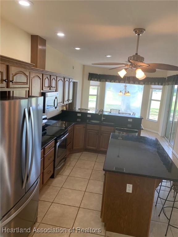 kitchen featuring a breakfast bar area, stainless steel appliances, dark countertops, a sink, and a peninsula