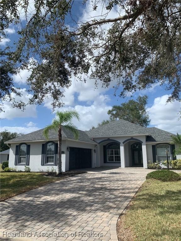 ranch-style home with a garage, a front lawn, decorative driveway, and stucco siding