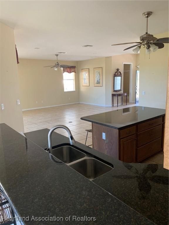 kitchen with light tile patterned floors, dark countertops, ceiling fan, open floor plan, and a sink