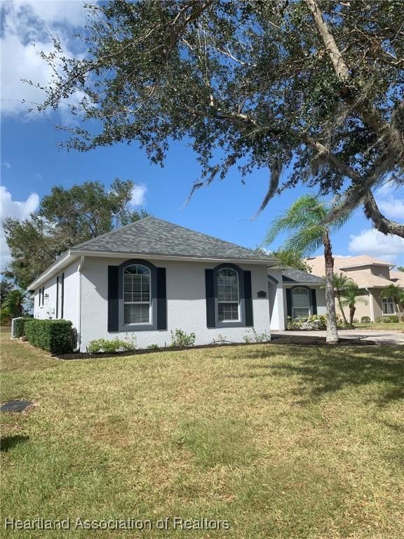 ranch-style house with a shingled roof, a front lawn, and stucco siding