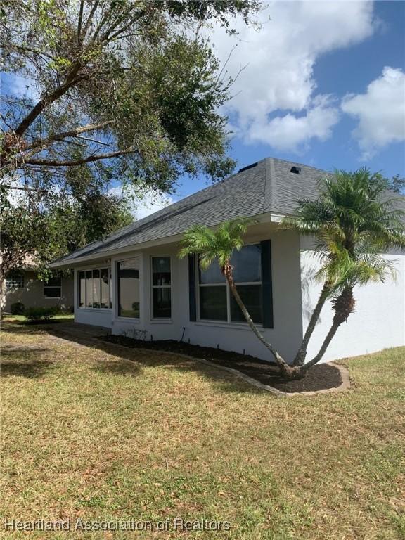 view of side of home with a yard, a shingled roof, and stucco siding