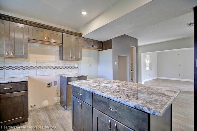 kitchen with light hardwood / wood-style floors, backsplash, dark brown cabinets, light stone counters, and a center island