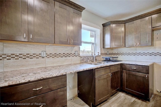 kitchen featuring tasteful backsplash, sink, dark brown cabinetry, light wood-type flooring, and light stone counters