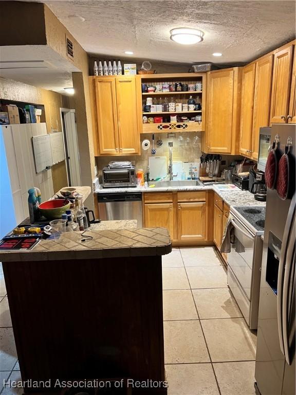 kitchen with tile countertops, sink, a textured ceiling, light tile patterned flooring, and stainless steel appliances