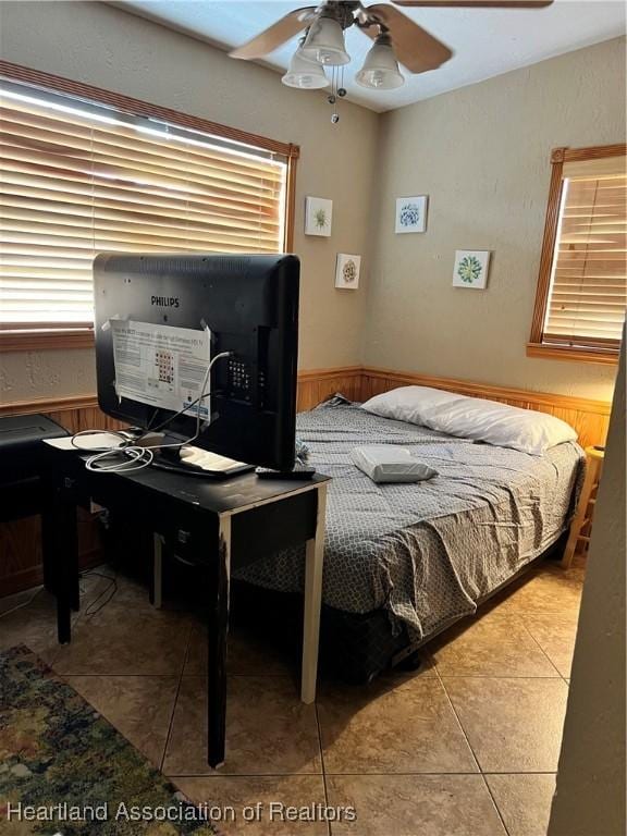 tiled bedroom featuring ceiling fan and wood walls