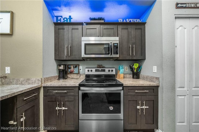 kitchen featuring a textured wall, stainless steel appliances, dark brown cabinets, and light countertops