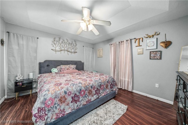 bedroom with ceiling fan, a tray ceiling, baseboards, and wood finished floors