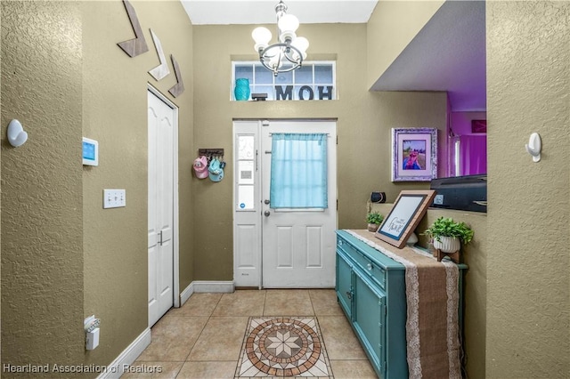 foyer entrance featuring baseboards, an inviting chandelier, light tile patterned flooring, and a textured wall