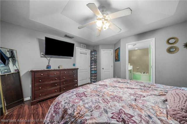 bedroom featuring visible vents, dark wood-type flooring, a ceiling fan, ensuite bathroom, and a raised ceiling