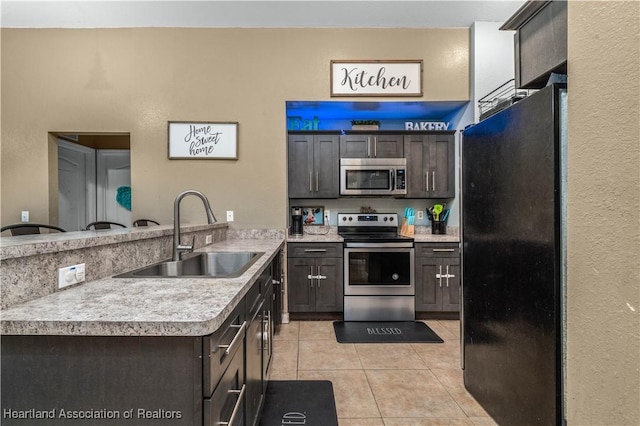 kitchen with light countertops, light tile patterned floors, appliances with stainless steel finishes, a peninsula, and a sink